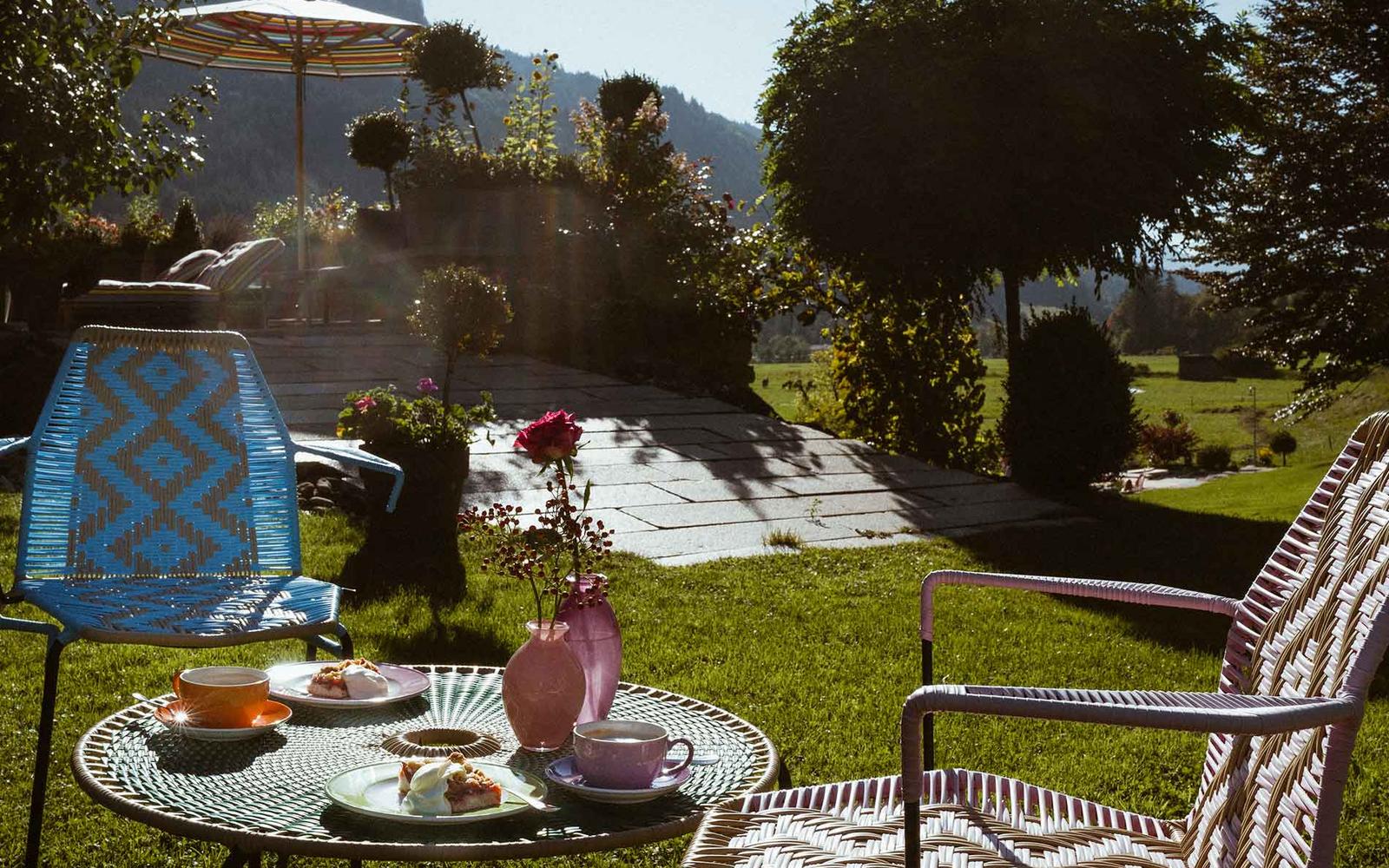 Bunte gedeckter Gartentisch mit Kuchen und Kaffee in der Sonne