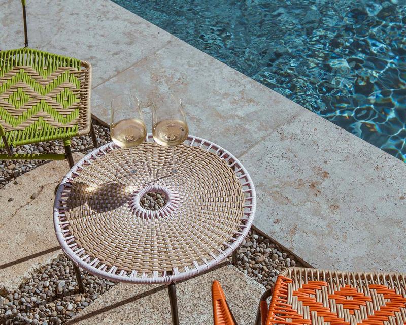  Poolrand mit Gartenmöbel im Vordergrund und Weingläser auf dem bunten gewebten Tisch 